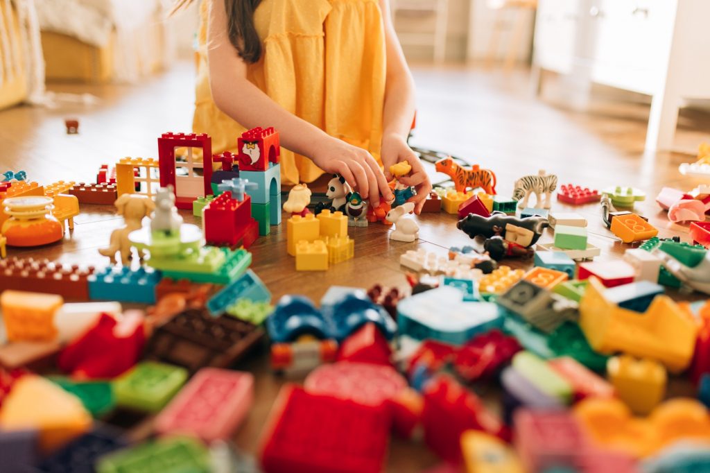 Little toddler girl playing with Lego blocks at home alone